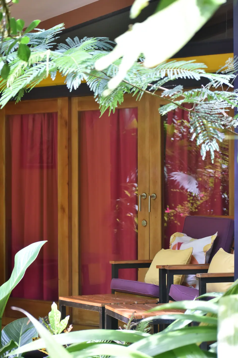 Red doors and a purple armchair on a casita terrace framed by tropical leaves